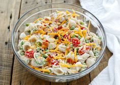 a glass bowl filled with pasta salad on top of a wooden table