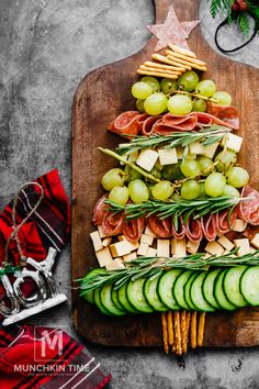 a wooden cutting board topped with cucumbers, cheese and crackers next to a christmas tree shaped platter