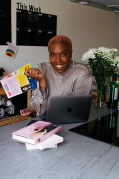 a woman sitting at a table with a laptop computer and books on the counter in front of her