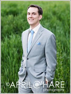 a man in a gray suit and blue tie standing in tall grass with his hands in his pockets