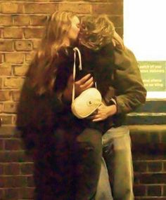 a man and woman kissing while sitting on a bench in front of a brick wall