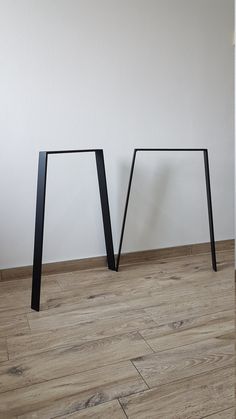 two black metal legs on the floor in front of a white wall and wooden floor