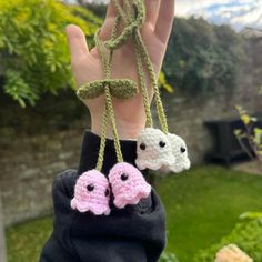 a hand holding three small crocheted items in the shape of two sheeps