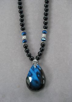 NOTE: Fire Agates are natural volcanic stone and they are not perfect due to the nature of the stone. However, they are very pretty! The pendant is unusual and it is thicker than most because it comes from volcanic rock. This is a pretty teardrop shaped Black and Blue Fire Agate Pendant Necklace.   The beads in the necklace are genuine black agate with blue crystal beads that pick up the colors of the pendant with silver crystal accents.   The pendant is polished. The pendant measures 2 inches long x 1 1/2 inches wide.  This is a unique one of a kind necklace.  It's 16 inches long and adjustable to 20.  All my jewelry is unique and one of a kind. Similar quality jewelry is priced at double. I source the stone pendants from all over the world. All pendants and necklaces are made with semipr Blue Crystal Beads, Agate Pendant Necklace, Volcanic Stone, Volcanic Rock, Fire Agate, Pretty Jewelry, Black Agate, Blue Fire, Silver Crystal