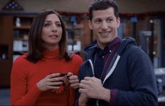 a man and woman standing next to each other in front of a christmas tree with lights