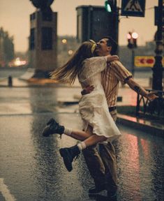 a man and woman dancing in the rain on a city street with traffic lights behind them