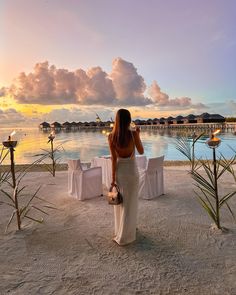 a woman is standing on the beach looking out at the water and holding a purse