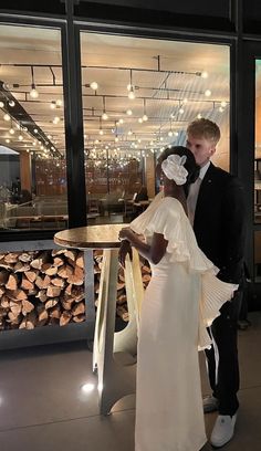 a man and woman standing next to each other in front of a pile of logs