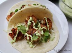 two shrimp tacos with guacamole and sour cream sauce on a white plate