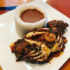 a white plate topped with food next to a bowl of dipping sauce on top of rice