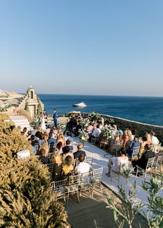 a group of people sitting on top of a roof next to the ocean and trees