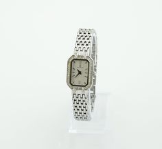 This silver-colored watch boasts a rectangular case surrounded by stones, adding a touch of elegance and sparkle. The grey metallic dial is also adorned with stones, enhancing its luxurious appeal. Paired with a classic metal bracelet, the watch strikes a balance between simplicity and brilliance. It's a sleek, bright, and elegant accessory that stands out for its understated glamour and sophistication. Dimensions: Bracelet Length: up to 16 cm (6.3 inches) - adjustable Case Width: 1.7 cm (0.4 inches) Case Height: 2.3 cm (0.9 inches) Bracelet Width: 1 cm (0.4 inches) Condition: The watch is in good condition, with minor wear on the bracelet and a tiny chip on the glass between the 3 and 4-hour marks, details in the photo. All presented watches are tested and in working condition, also equip Elegant Rectangular Diamond Watch For Anniversary, Elegant Rectangular Diamond Watch As Gift, Elegant Rectangular Diamond Watch For Gift, Elegant Rectangular Diamond Watch Gift, Elegant Rectangular Watches For Anniversary, Elegant Silver Jewelry With Diamond Hour Markers, Classic Silver Rectangular Jewelry And Watches, Elegant Rectangular Analog Jewelry And Watches, Rectangular Polished Diamond Watch As Gift