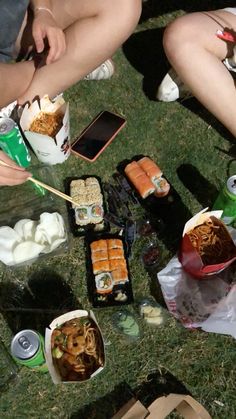 people sitting on the grass eating sushi and chopsticks at an outdoor gathering