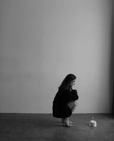 a woman sitting on the floor in front of a window next to a toilet paper dispenser