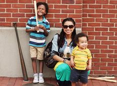 a woman and two children standing next to a brick wall with a baseball bat on it