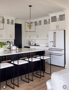 a kitchen with white cabinets and black countertops is pictured in this image, there are four stools at the center of the island