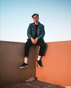 a man sitting on top of a wall with his legs crossed and wearing black sneakers