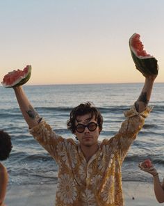 a man holding two slices of watermelon in his hands while standing on the beach