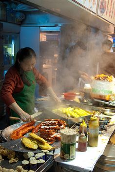 a woman cooking food on top of a grill next to other foods and condiments