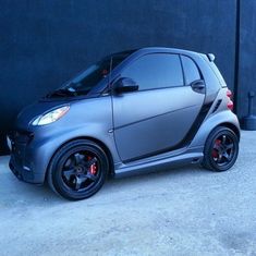 a smart car parked in front of a black wall with red rims on it