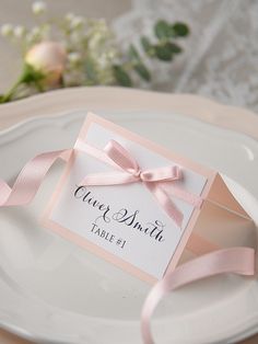 a place card with a pink ribbon tied around it on top of a white plate