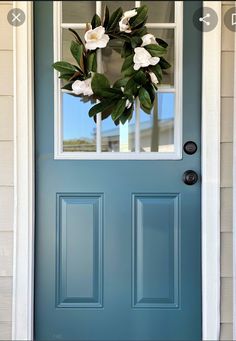 a blue front door with a wreath on the top and two white flowers hanging from it