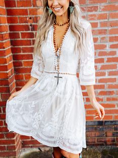 a woman standing in front of a brick wall wearing a white dress and cowboy boots