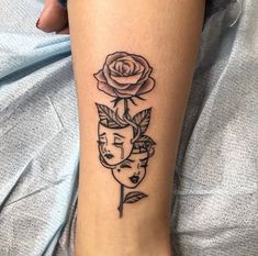 a woman's leg with a rose and two faces tattoo on her left calf