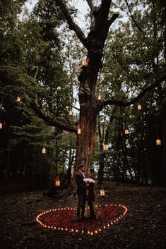 a couple standing in front of a tree with candles on the ground and lights hanging from it