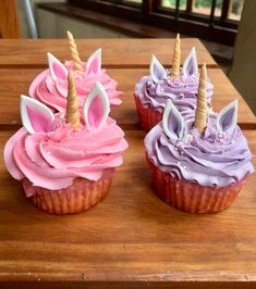 three cupcakes with pink frosting and unicorn horn decorations on top of a wooden table