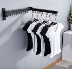 there are four shirts hanging on the rack in front of a white wall and a potted plant next to it