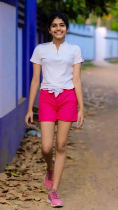 a woman in pink shorts and white shirt walking down the street with her hand on her hip