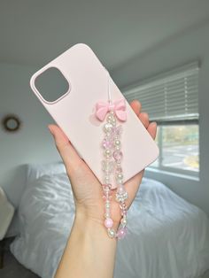 a person holding up a pink phone case with pearls and bows on the side,