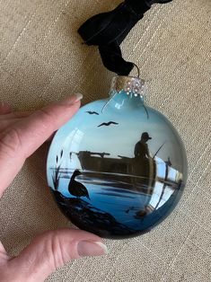 a hand holding a blue glass ornament with a man fishing on the water