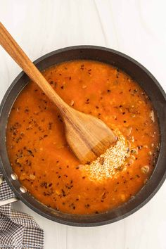 a wooden spoon in a pan filled with tomato soup on a white tablecloth next to a plaid napkin