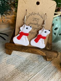 a pair of white polar bear earrings sitting on top of a wooden stand next to a christmas tree