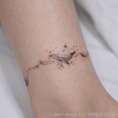 a small tattoo on the ankle of a woman's foot with a whale and stars