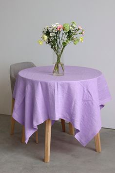 a vase with flowers sitting on top of a table next to a gray chair and grey wall