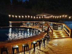 an outdoor deck with lights and bar stools next to a swimming pool at night