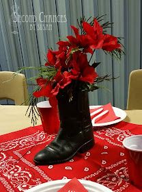 a table set for christmas with red flowers in a boot and napkins on it