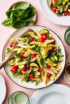 a white plate topped with pasta and veggies on top of a pink table