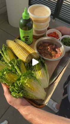 a person holding a sandwich with lettuce, corn and sauces on it