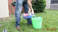 a man is pouring water into a green bucket on the grass in front of a house