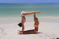 two women in bikinis doing yoga on the beach