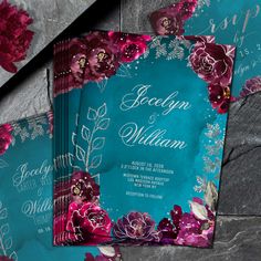 two wedding cards with flowers on them sitting next to each other in front of a stone wall