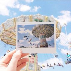 a person holding up a polaroid photo in front of an amusement park carousel ride