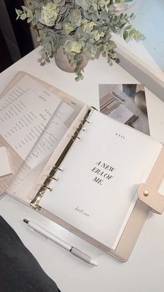 an open planner book sitting on top of a table next to a vase with flowers