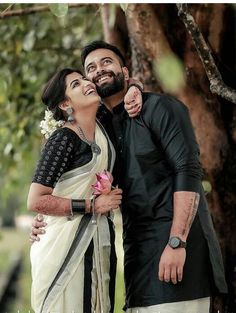 a man and woman standing next to each other in front of trees with their arms around each other