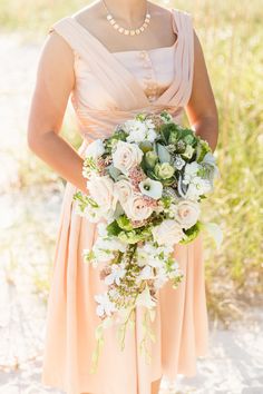 a woman in a dress holding a bouquet of flowers and greenery on the beach