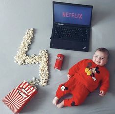 a baby laying on the floor next to popcorn and a laptop